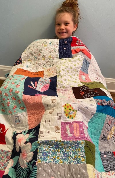 girl sitting on floor under baby clothes quilt by Too Cool T-shirt Quilts